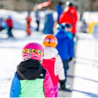Kids in ski gear lining up behind a ski pro on a mountain