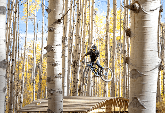 Biker in Snowmass Bike park rides over wooden feature in the fall at Aspen Snowmass