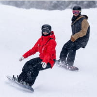 Snowboarder taking a lesson with a ski pro in a red jacket on a ski mountain