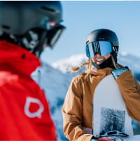 Snowboarder in brown jacket looking at a ski pro in a red jacket on a mountain