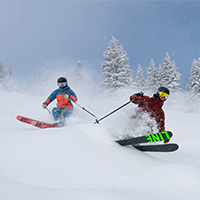 two skiers cruise down a bump run in deep powder