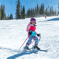 Little girls stops in front of camera on a snowy slope, with a big smile on her face, at Snowmass