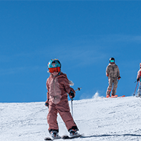 Little girl dressed in pink skis out in front of her family on a bluebird day, at Snowmass