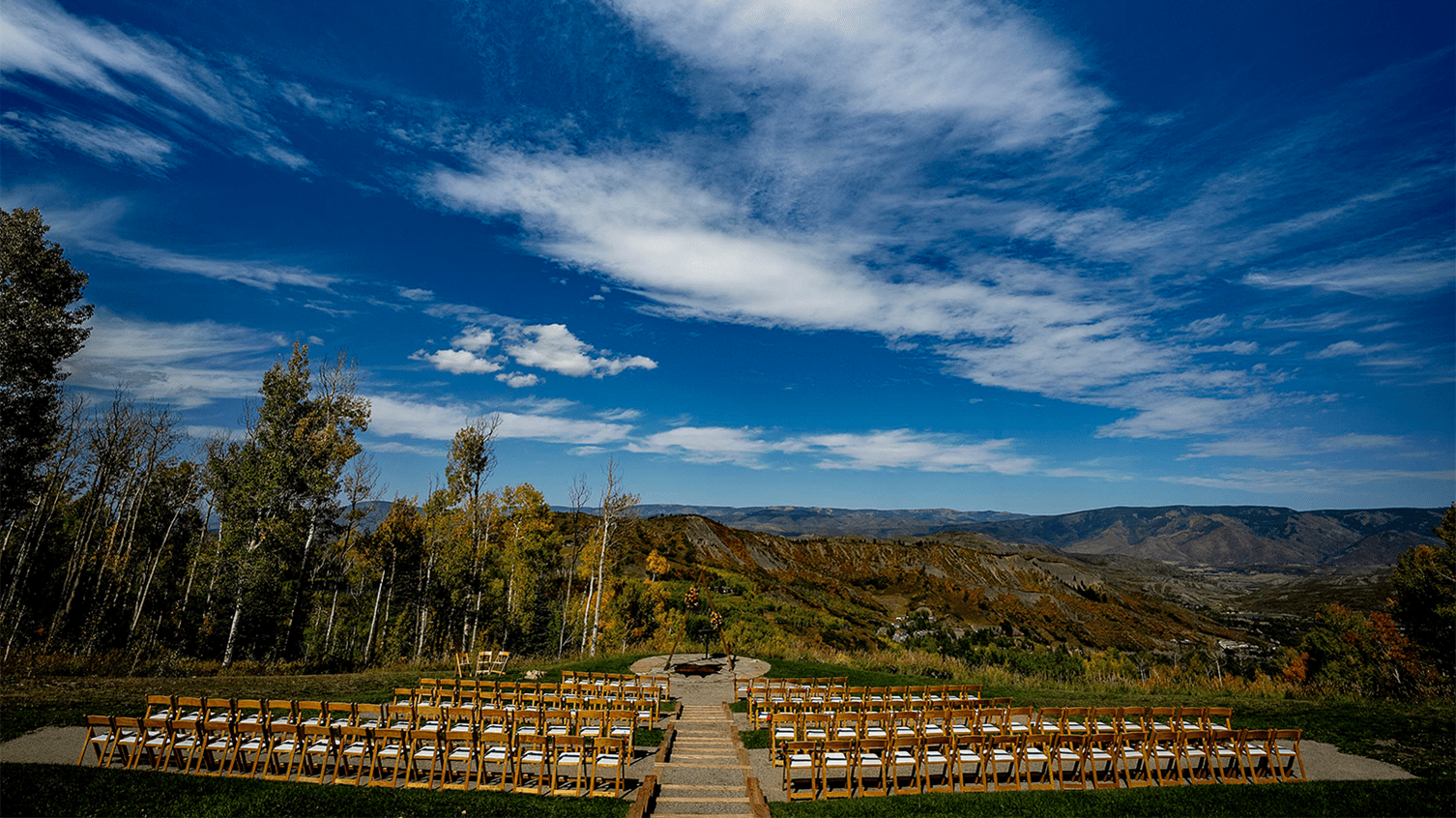 Empty wedding chairs lined up in front alter, before an outdoor wedding at Snowmass. Blue sky and light falls colors surround the space