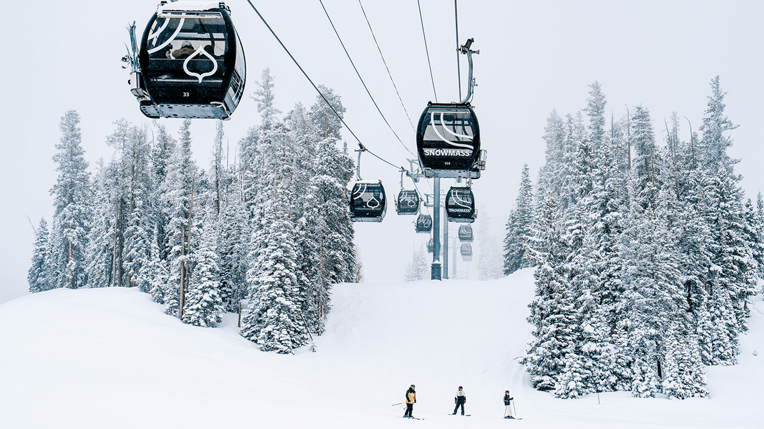 Snowmass Gondola on a cloudy day, skiers below the cars and snow coats the tree