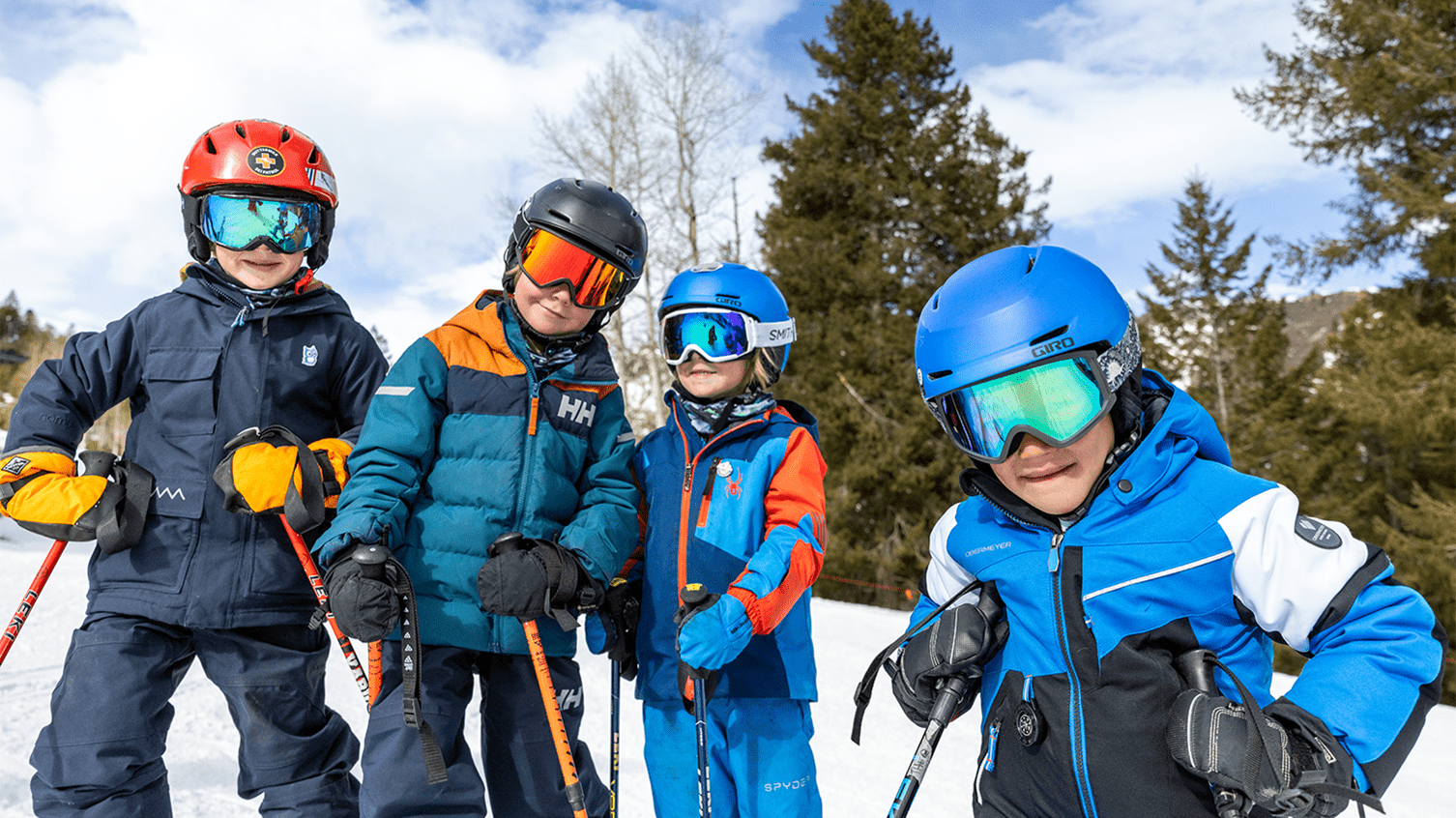 Four kids smile at the camera as they ski together on Aspen Highlands