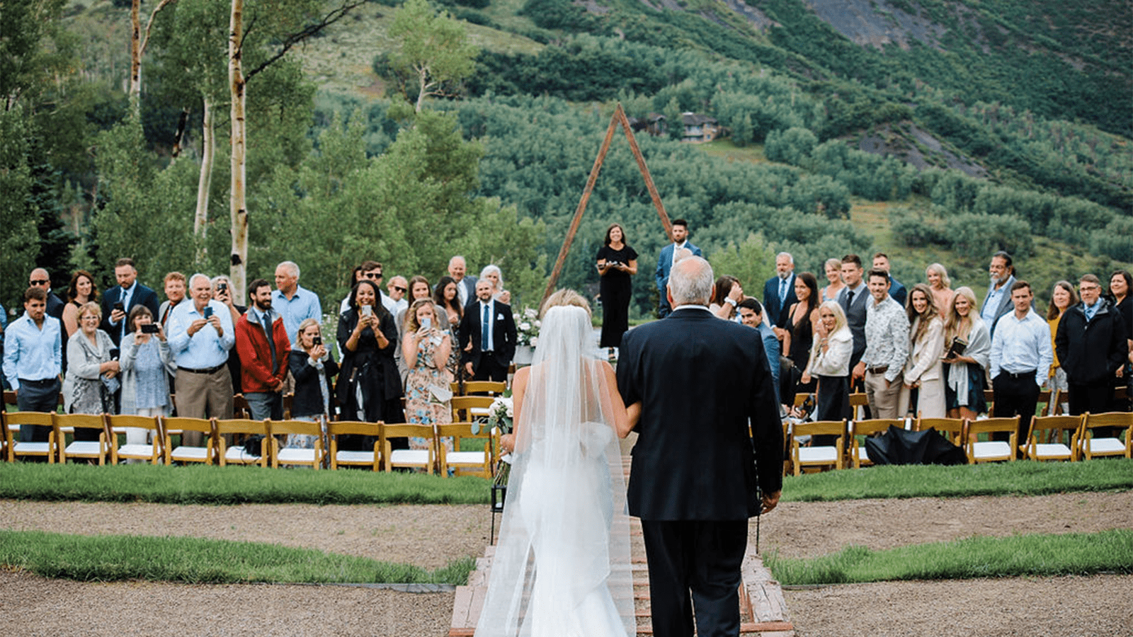 Bride walks down the isle with her father, guests look up at them from the seats