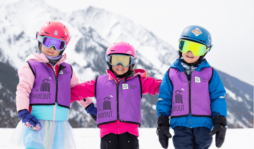 Three kids smile on the hills of buttermilk during their kids lesson at aspen snowmass