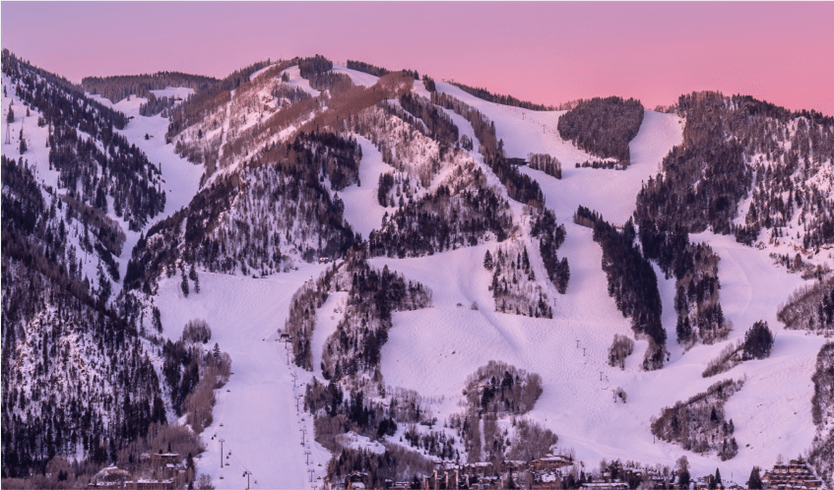 Aspen Mountain under pink skies, during ski season, with white runs lines by dark trees